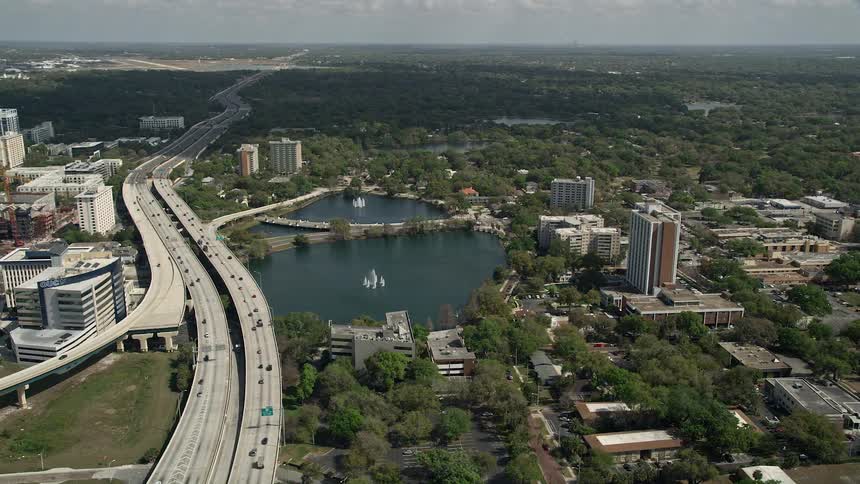 Aerial view of Lake Lucerne next to the expressway with traffic passing by and downtown Orlando in the background on a partly cloudy day