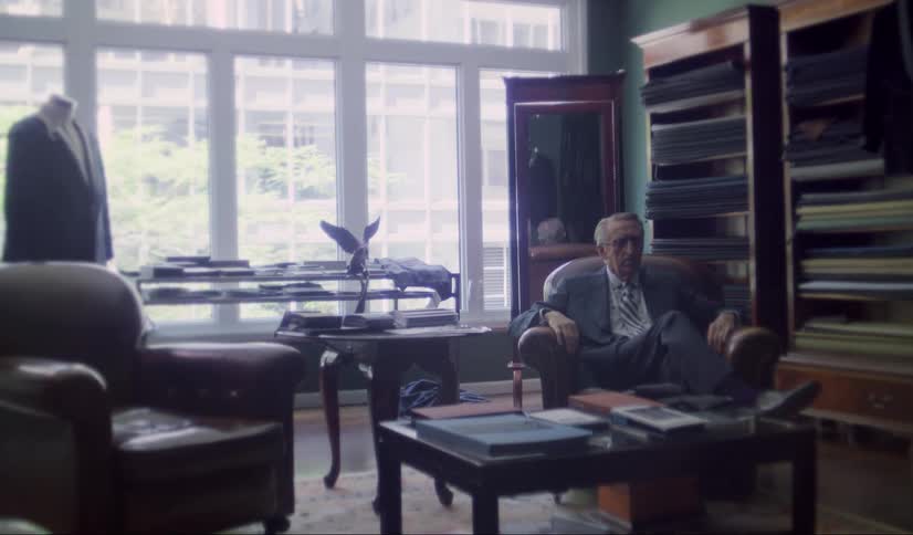 An older man in a suit and tie sitting in a chair in a store lobby