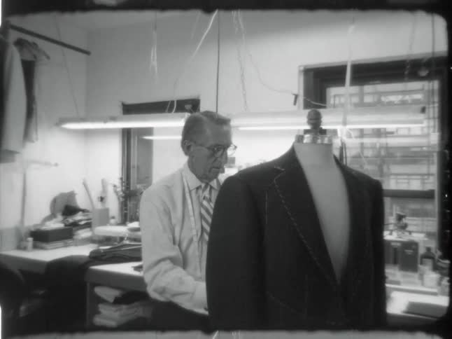 An elderly tailor measuring and manipulating a suit on a mannequin
