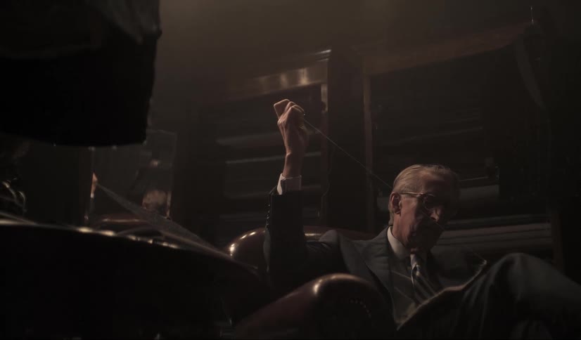 A tailor wearnig a formal suit sitting on a dimly lit room sewing