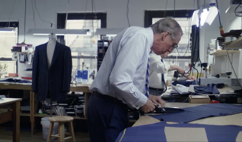 A suitmaker cuts fabric with scissors