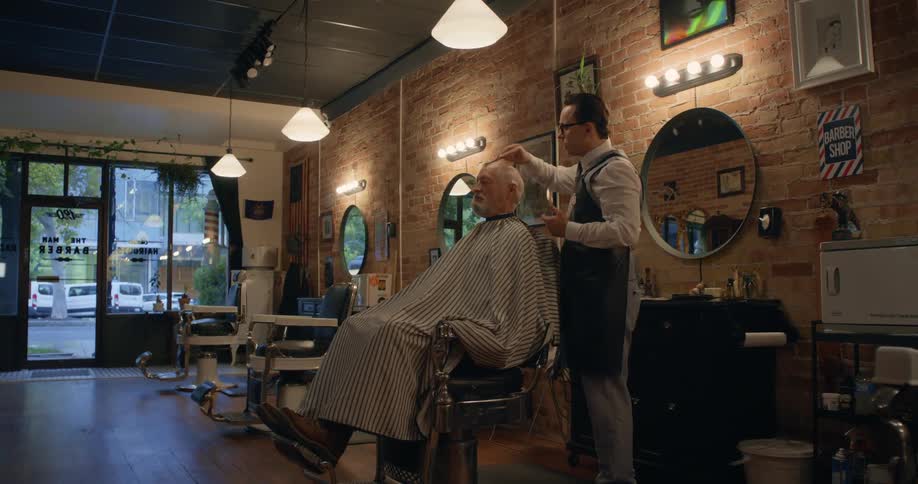 A barber combing a customers hair sitting in the chair in front of him