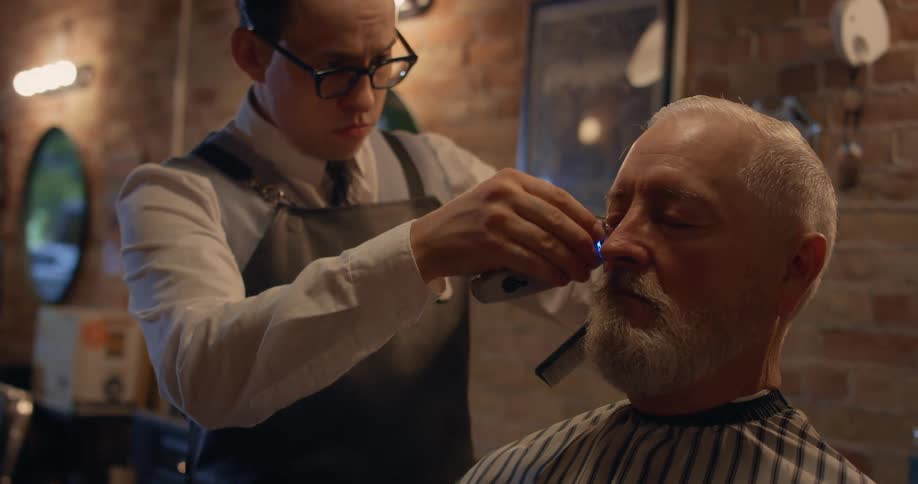 A barber cuts and combs the hair of a customer in a barber shop during the day