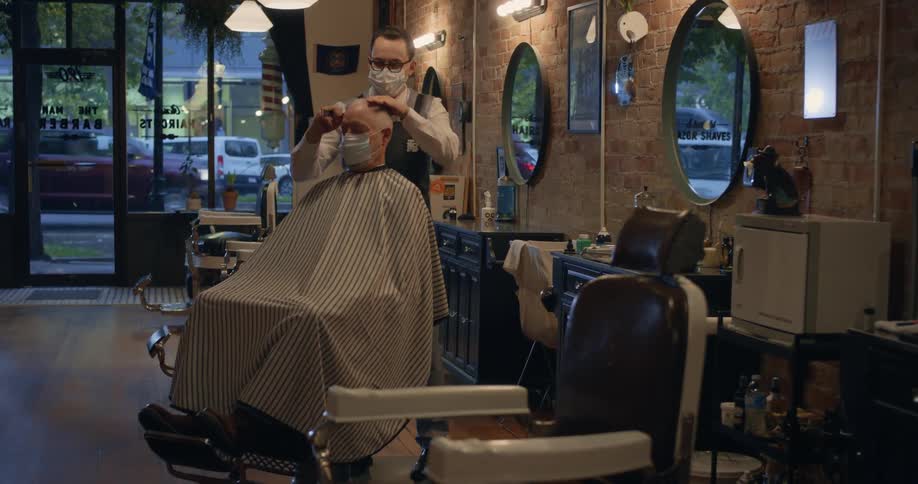 Hairdresser and client in the barbershop wearing face masks