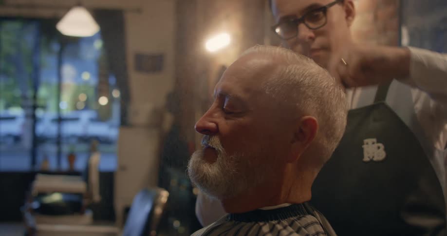 A happy man gets his hair combed by a barber