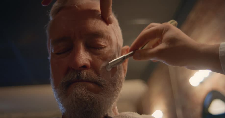 A man sits still as a barber shaves his face with a razor blade
