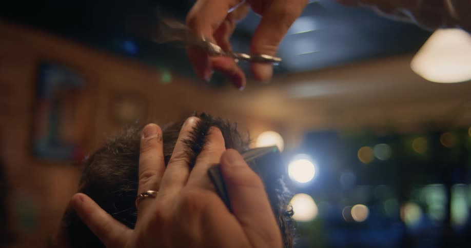 An up close of a barber using scissors and a comb on a mans hair