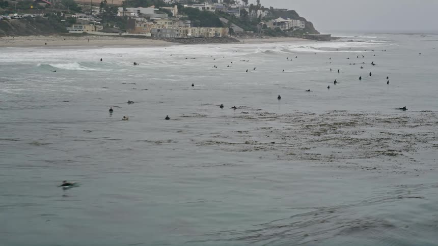 Approaching surfers riding waves in the Pacific Ocean off the coast of Malibu California captured from a high vantage point