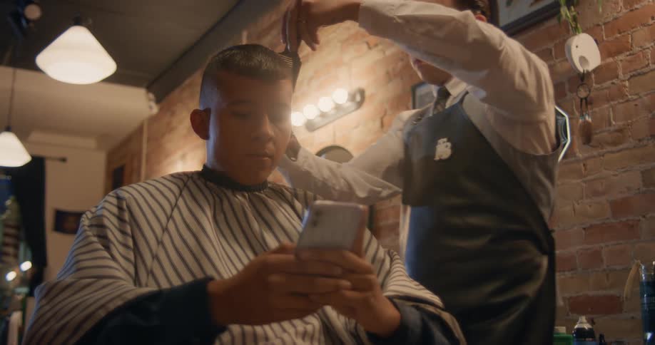 Hairdresser cuts the hair of a customer texting on the barber shop chair