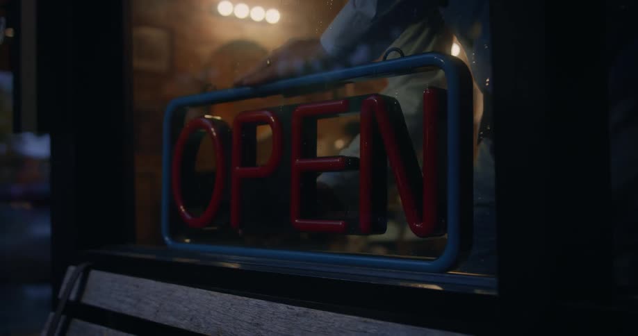 Man comes up and turns on neon open sign in the window of a bar and restaurant