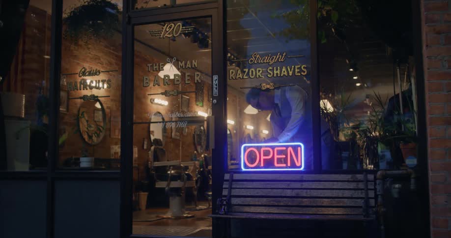 A barber turns on the neon open sign in a barber shop