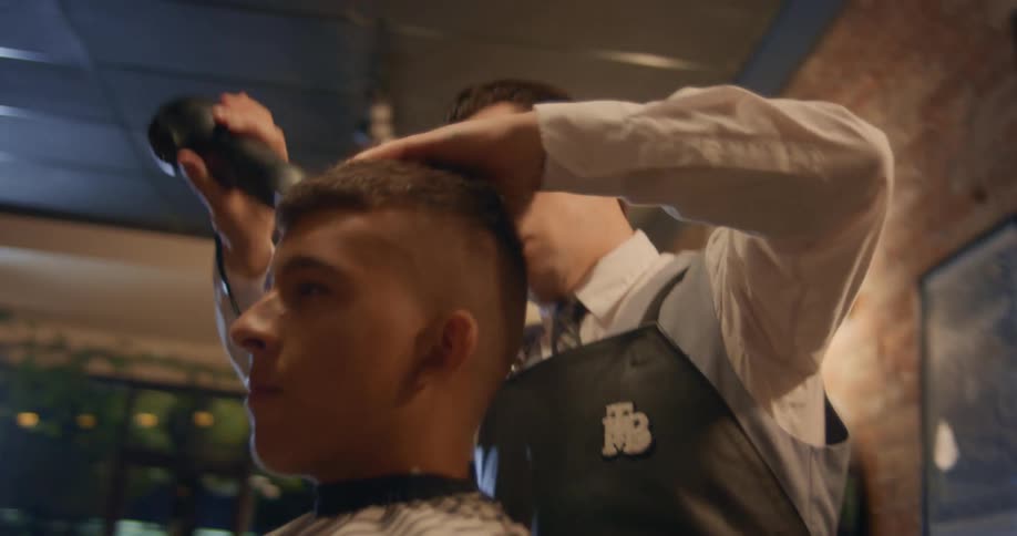 A barber is using a hair dryer to dry a young mans hair in a barber shop
