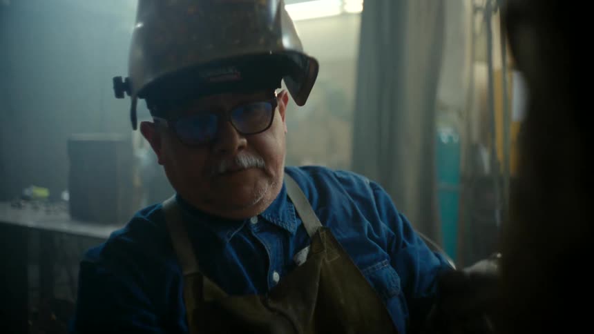 Close up of a man wearing a welders mask welding a large metal structure on his workshop