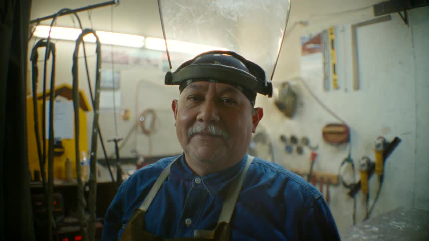 A man lifts the shield of his welding helmet and looks ahead