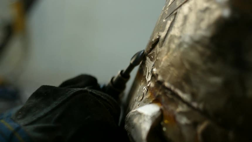 A man uses a dremel tool to shape a metal object