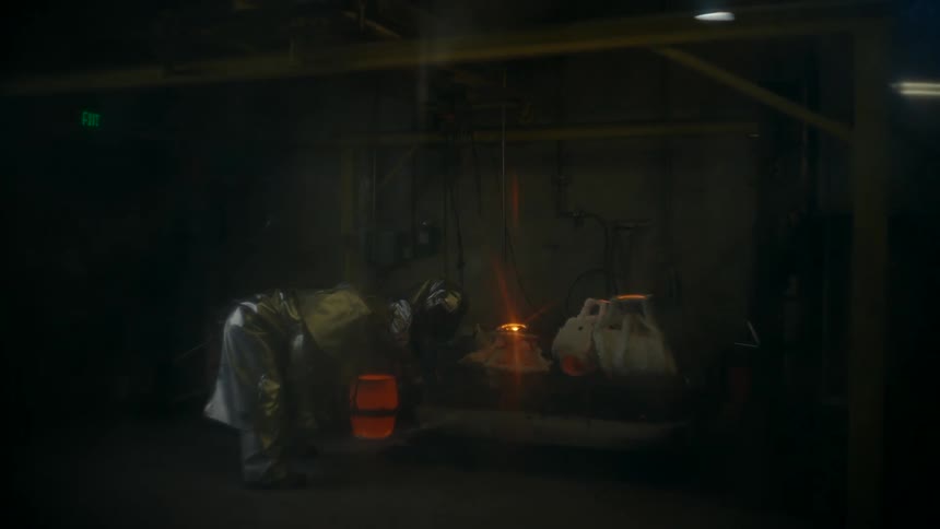 A person in a full body suit moving around and grabbing a hose near flames