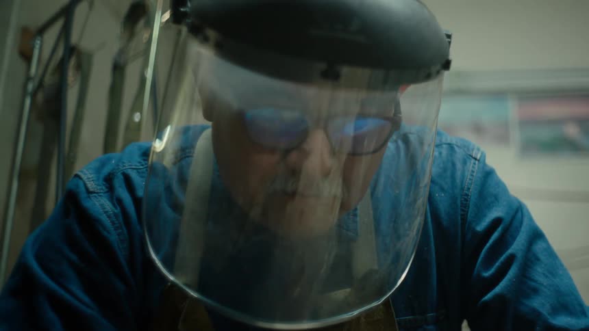 A man wearing a face shield and apron while working indoors