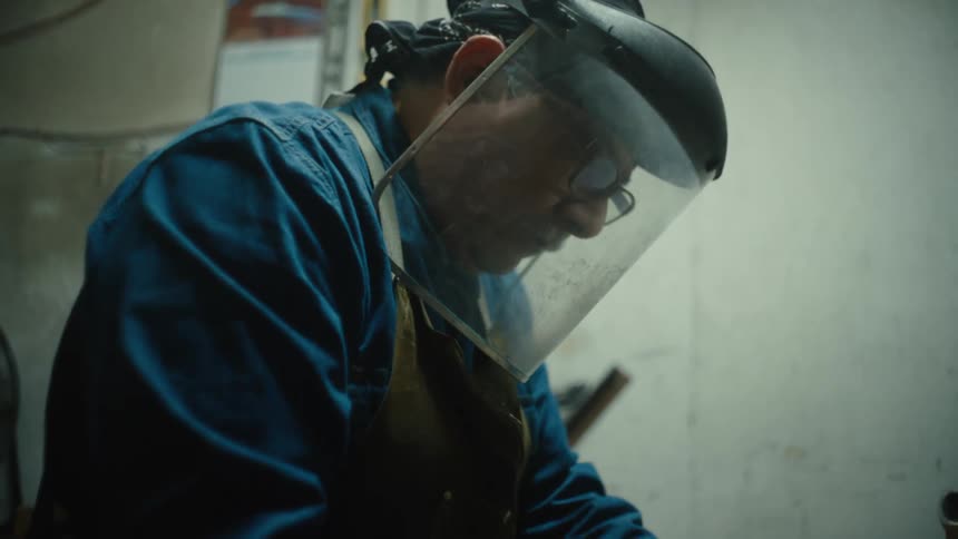Worker wearing face shield and apron works in workshop
