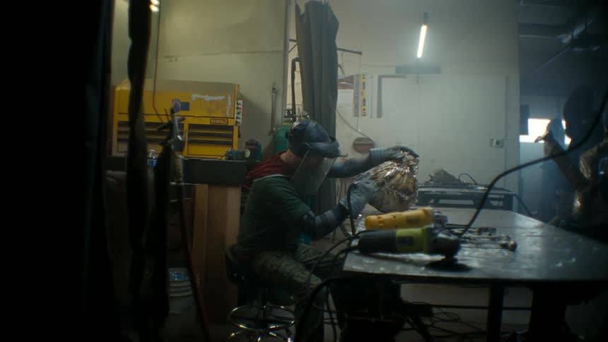 A man sitting on a stool using a tool to weld an object on a bench in front of him