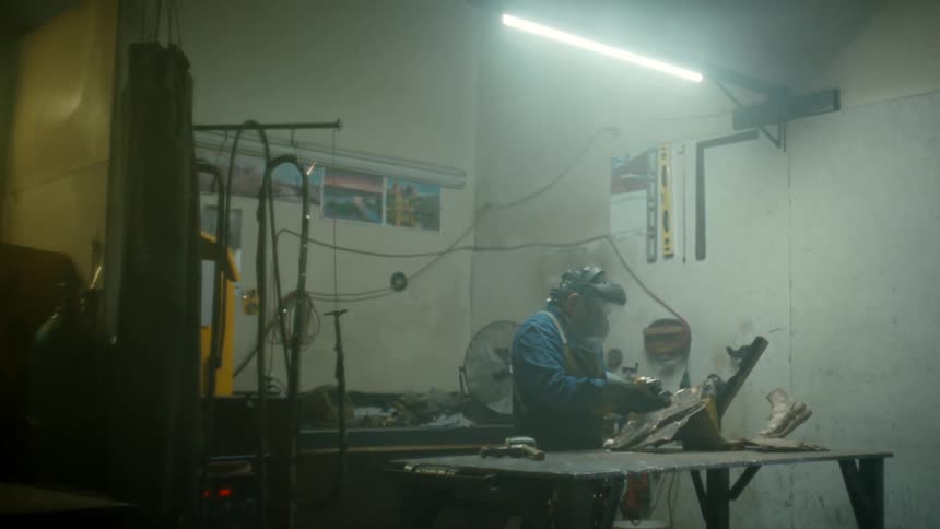 A man wearing a face shield standing at a work bench grinding creating sparks