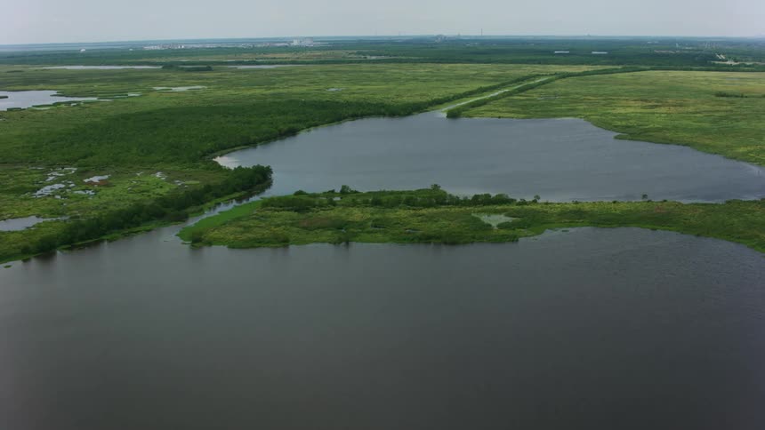 Aerial view of marshes vegetation channels and ponds as a drone flies over them on a cloudy day