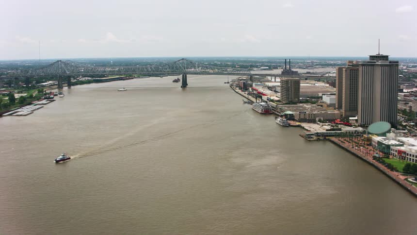 Ship leaves wake while moving down river away bridge spanning city