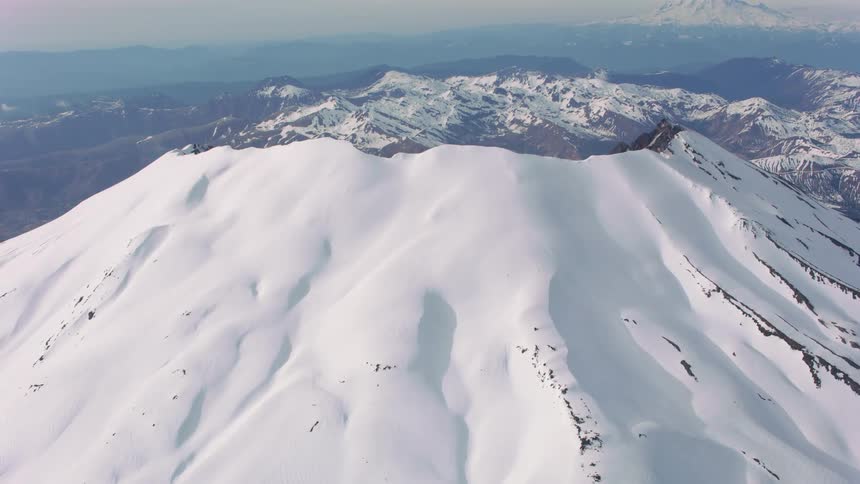 Ridges of a mountain poke through the snow and there are snow covered mountains in the distance under a hazy sky