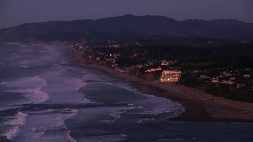Aerial view of sea waves crashing on the beach next to a coastal city at evening