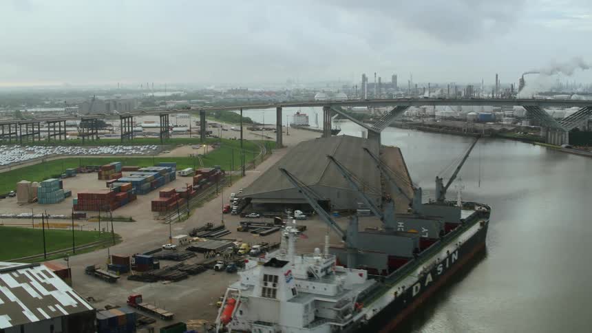 Traffic crosses river near docked freighter with multiple loading cranes