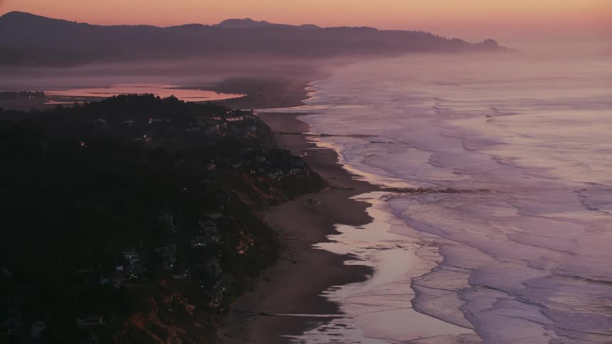 Aerial view of ocean waves washing on a beach next to a coastal town at evenin