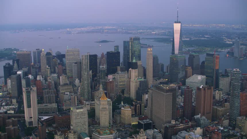 An aerial of a large city skyline at dusk with the ocean in the background with boats in the harbor