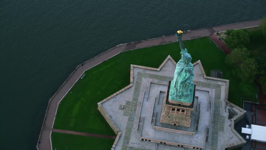 An aerial of the statue of liberty with calm waters surrounding it