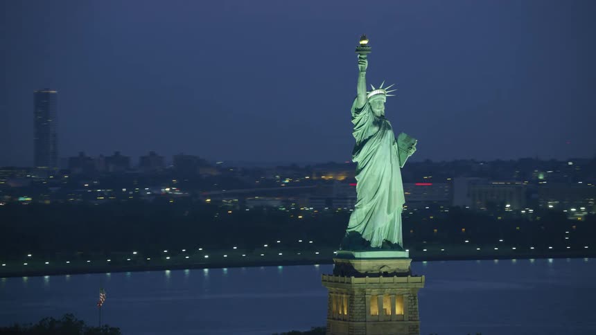 A statue standing tall close to a very big city during the night