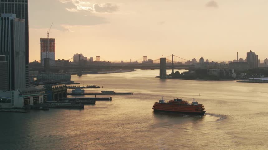 An aerial shot of a ship near a dock with a city skyline and bridge in the background