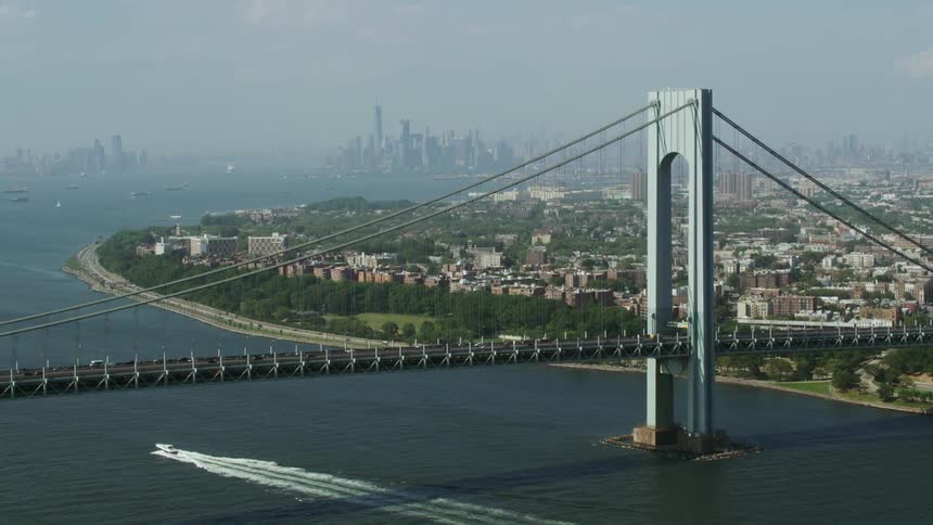 Aerial view of a boat sailing under a suspension bridge next to the city