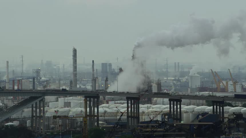 An aerial of smoke billowing into the air from factory chimneys with a bridge roadway near the factories