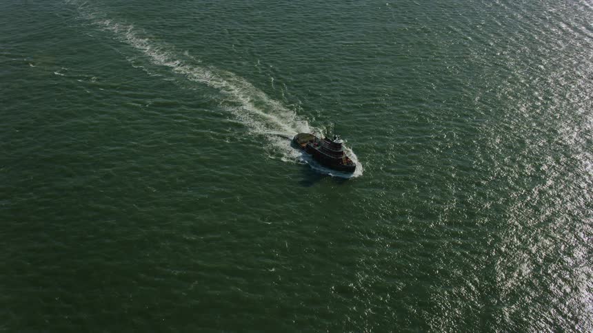 Aerial orbiting view of a red tugboat sailing