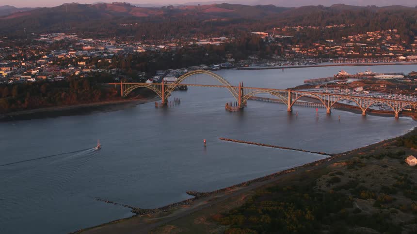 Aerial view of a boat sailing under an arched bridge near a coastal town