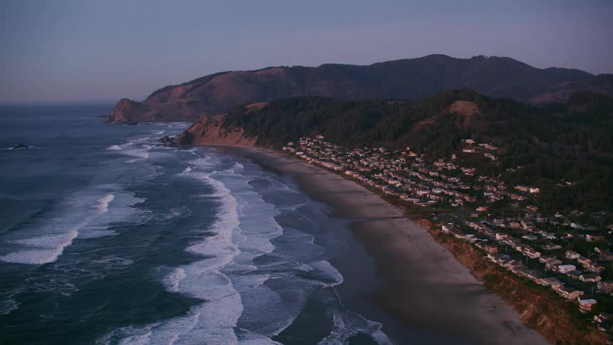Waves foam as they flow onto beach near town nestled against mountain