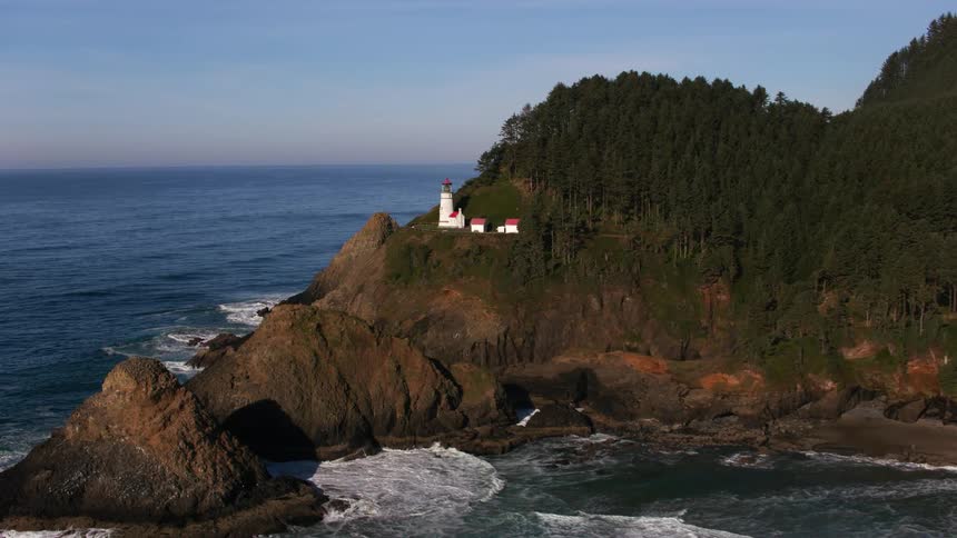 Waves crash onto a beach below a lighthouse