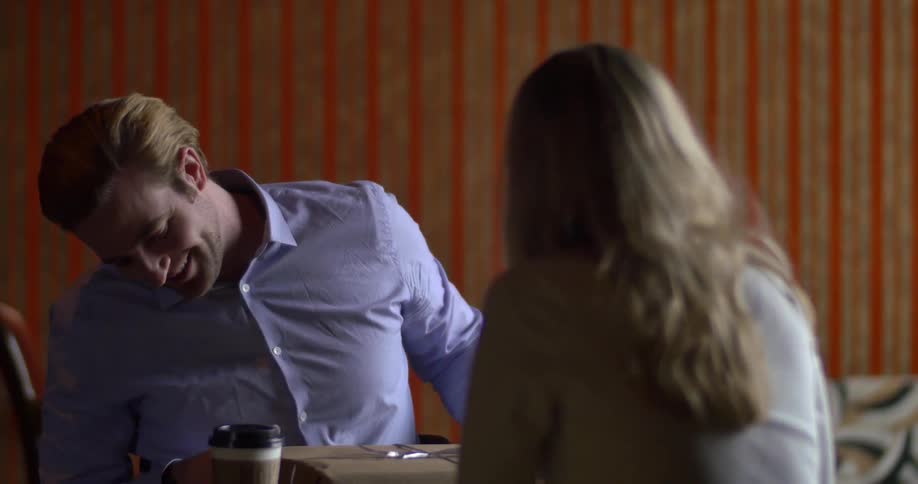 Couple sitting at a table as the man opens a present