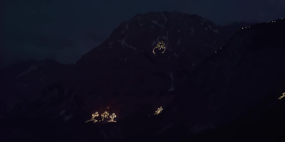 Electric lights form religious shapes on mountain side at night