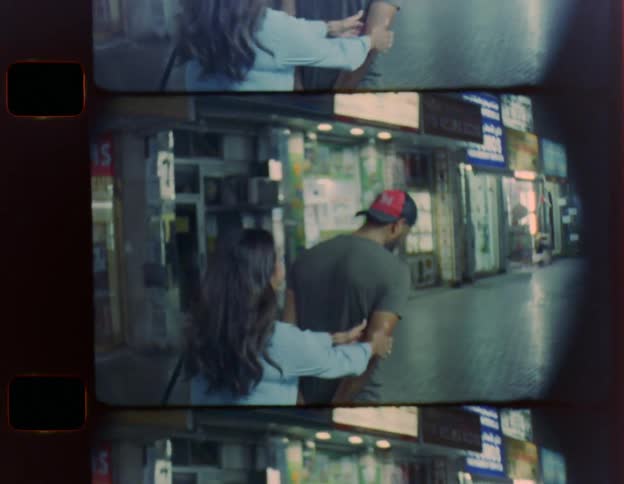 Man with t shirt cap and jeans and woman with light blue dress walk down the street playing with each other