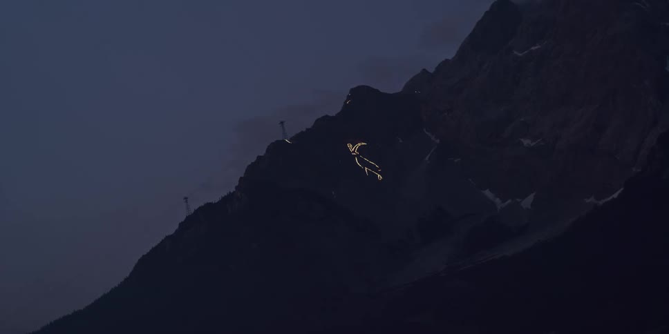 Utility towers stand on a mountain as clouds move overhead and as the sky becomes dark a glowing discharge moves on the mountainside