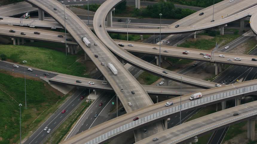 Traffic flows along overlapping overpasses and highways near buildings and lake