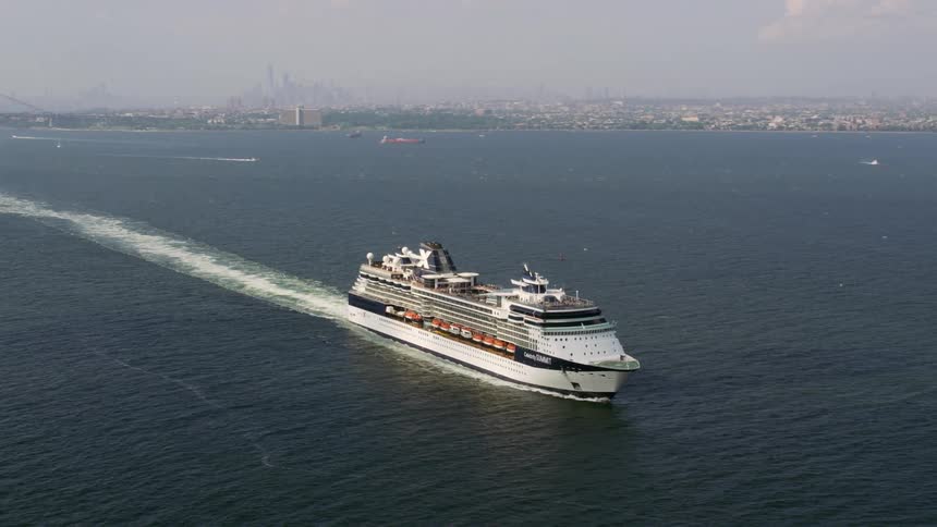 An ocean liner travelling a body of water and passing a city