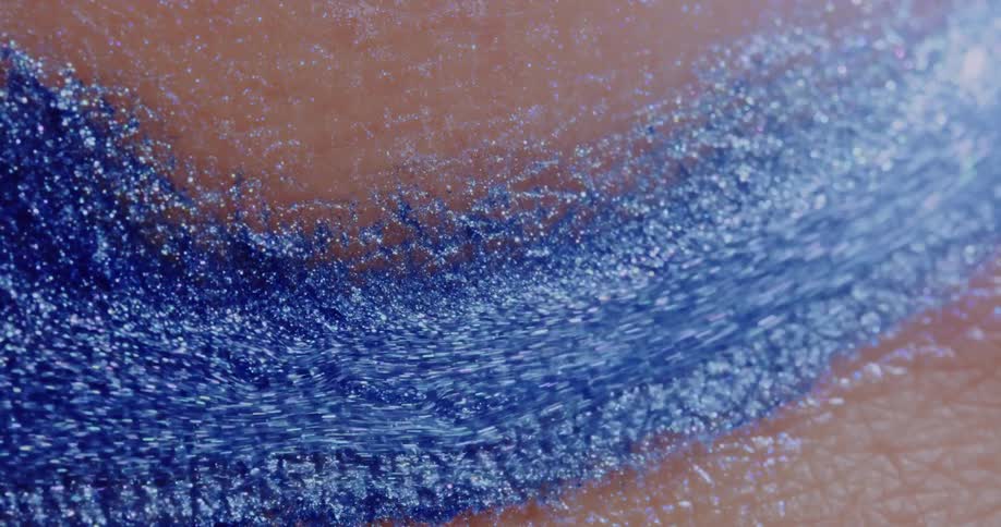 A strip of blue glitter liquid sparkles as it flows over a pink textured surface