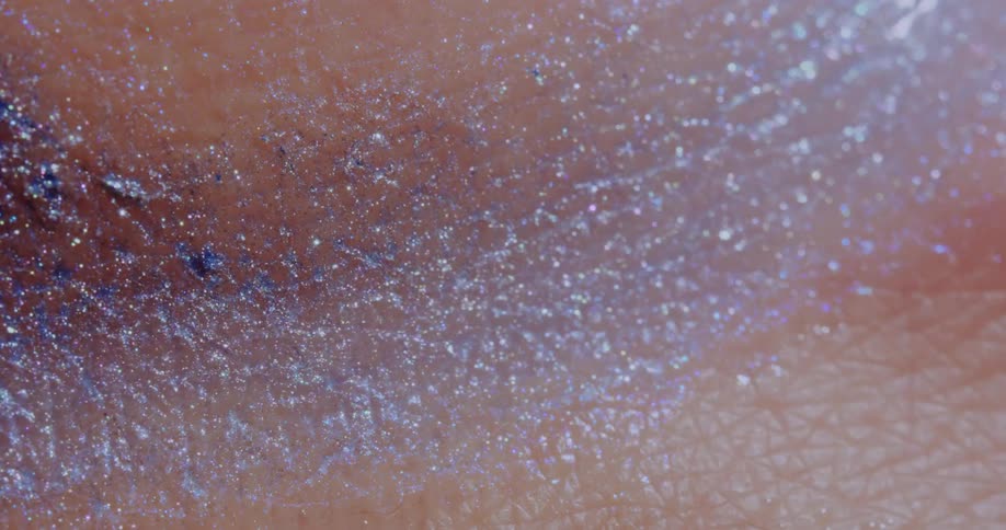 A sparkling glittering liquid substance moves over a pink textured surface as it twinkles in the light