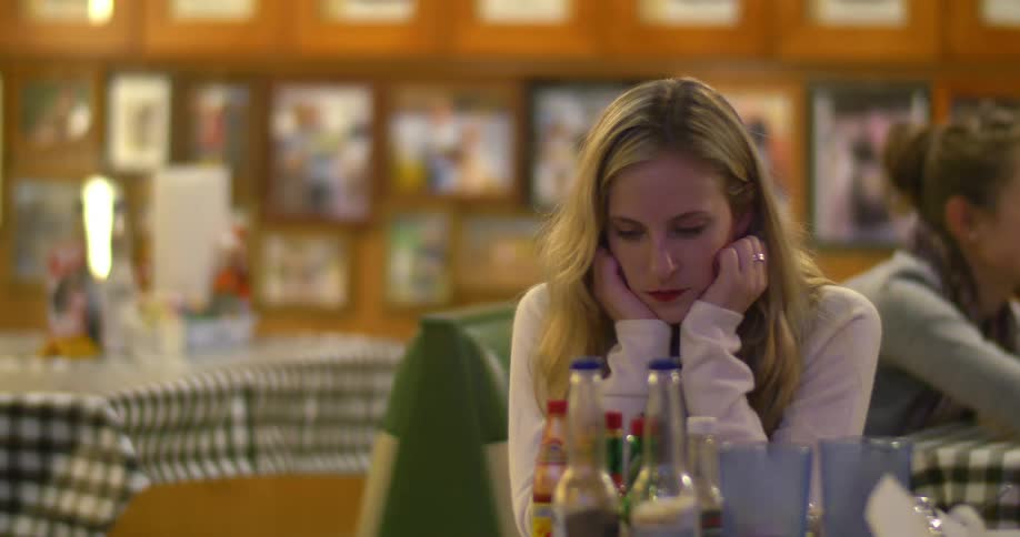 A man and a woman sitting at a table in a cafe and the man gets up and walks away