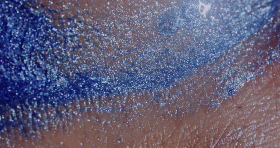 Blue glitter in liquid streams across the skin of a person